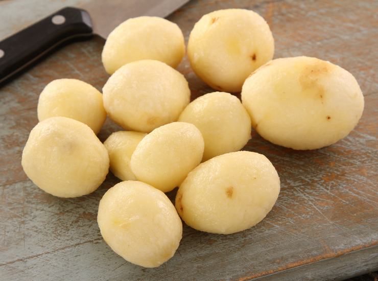 Le mani del bambino eseguono sbucciare le patate usando un pelapatate.  attrezzatura speciale per le verdure cotte.